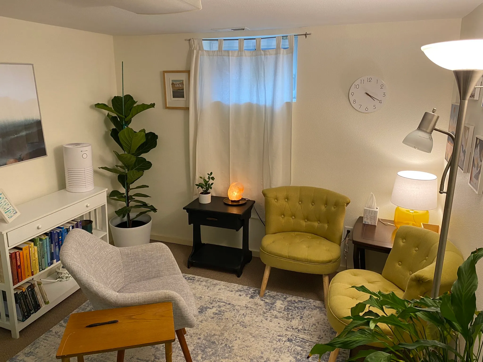 Brandon’s counseling room: two olive tufted armchairs and a soft grey chair arranged around a patterned rug, with a bookshelf, a fiddle-leaf fig, and a warm salt lamp.