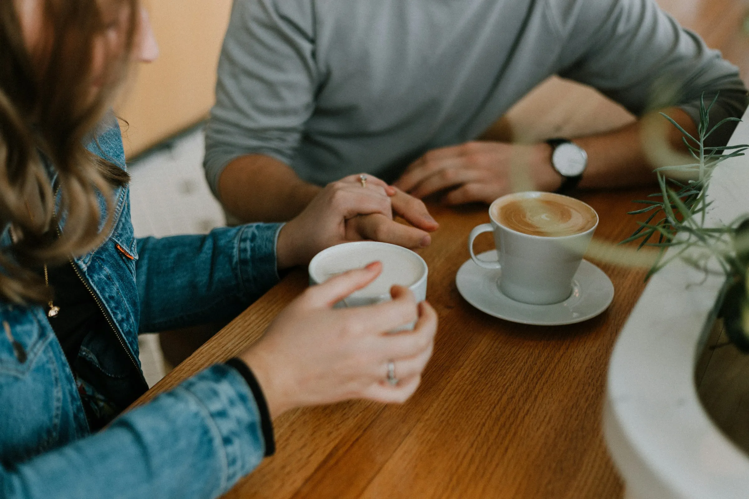 Two people holding hands across a wooden table, coffee cups beside them.